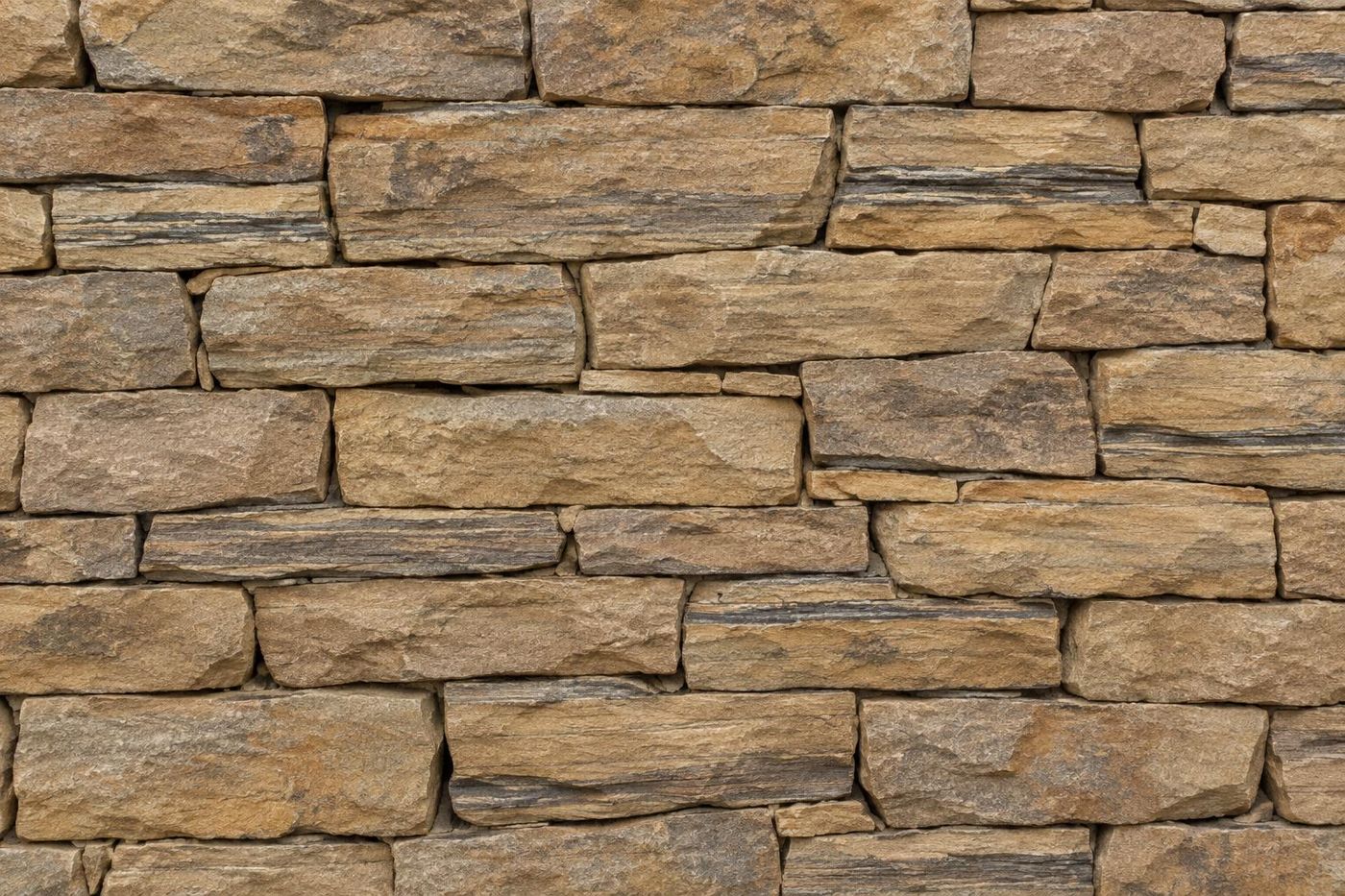 Flat straight-on texture of a drystone sandstone wall face, stones filling the frame edge to edge.