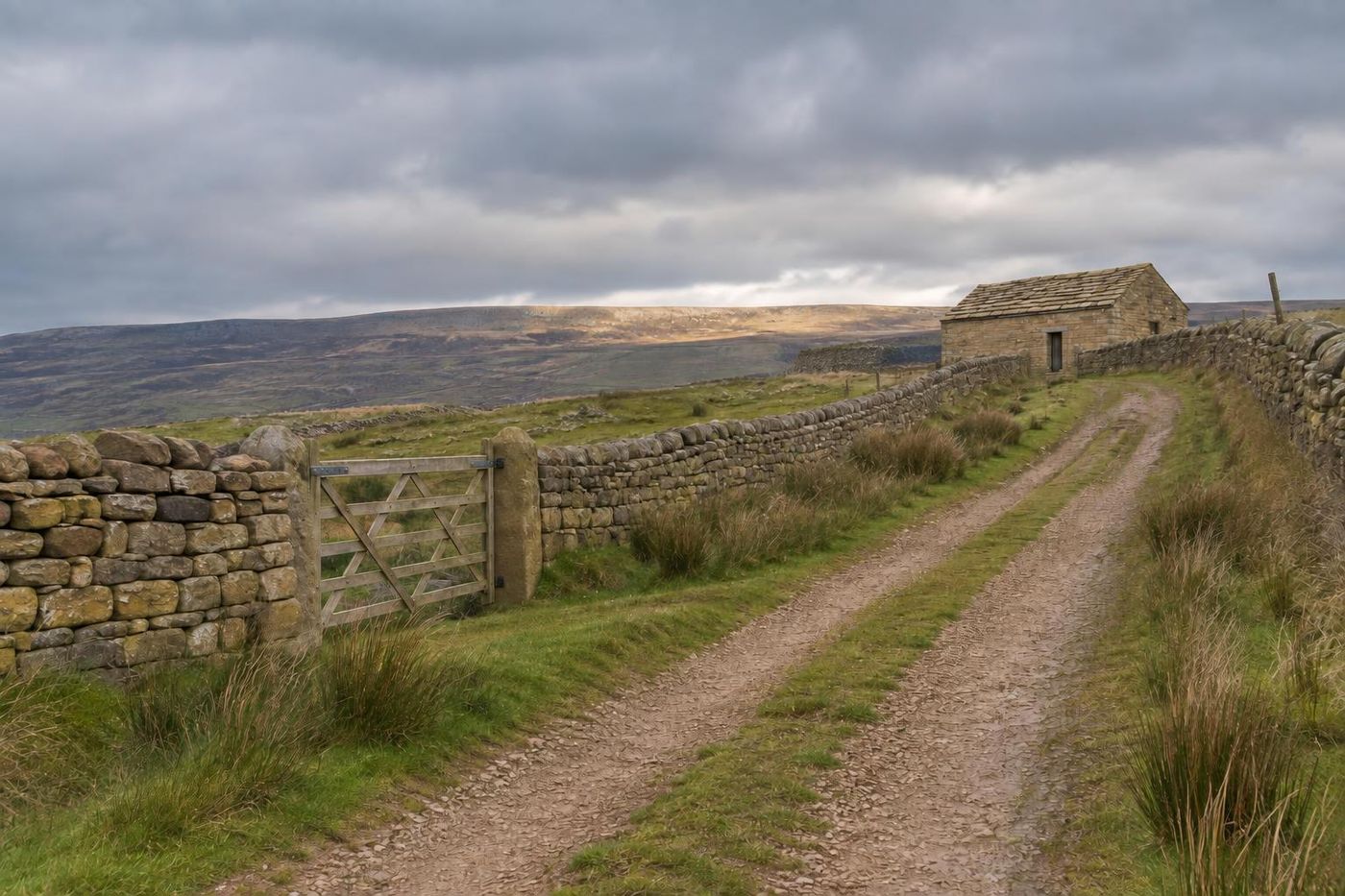 A firm crushed sandstone farm track climbing rough upland pasture between drystone walls to a stone field barn with a heavy buff-grey stone-slate roof, moody fell sky.